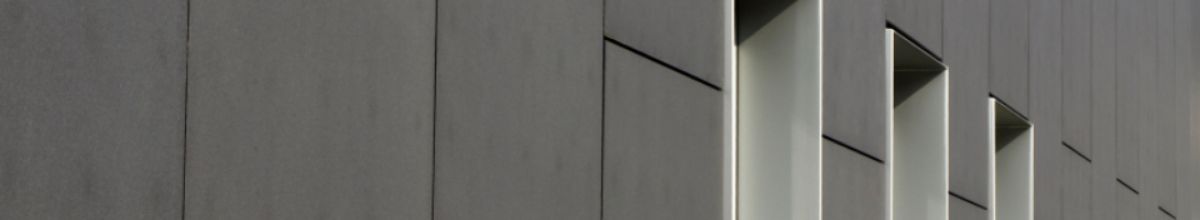 Plain grey concrete facade of an office building, its deep window reveals catching the light.