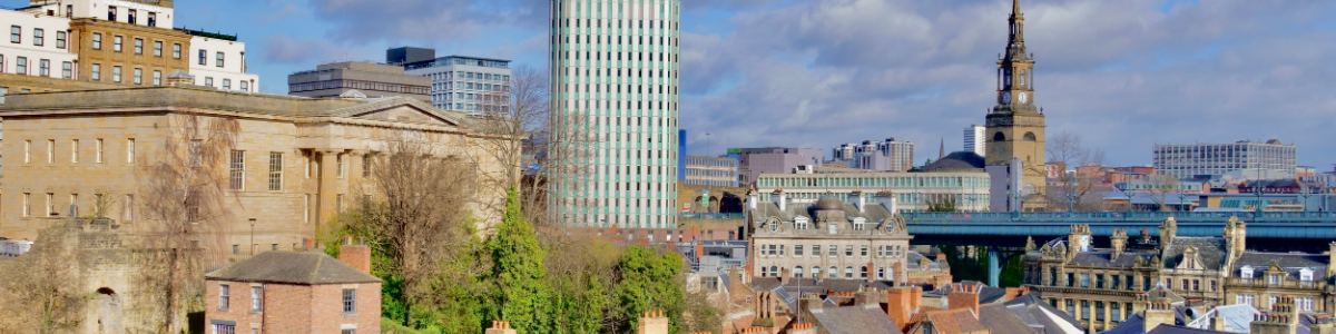 Rooftops, church spires and office towers of a British city centre under a broken sky.