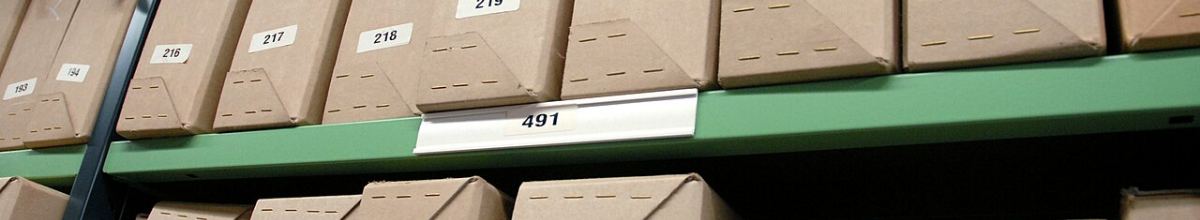 Numbered archive boxes on a green metal shelf, one label reading 491.